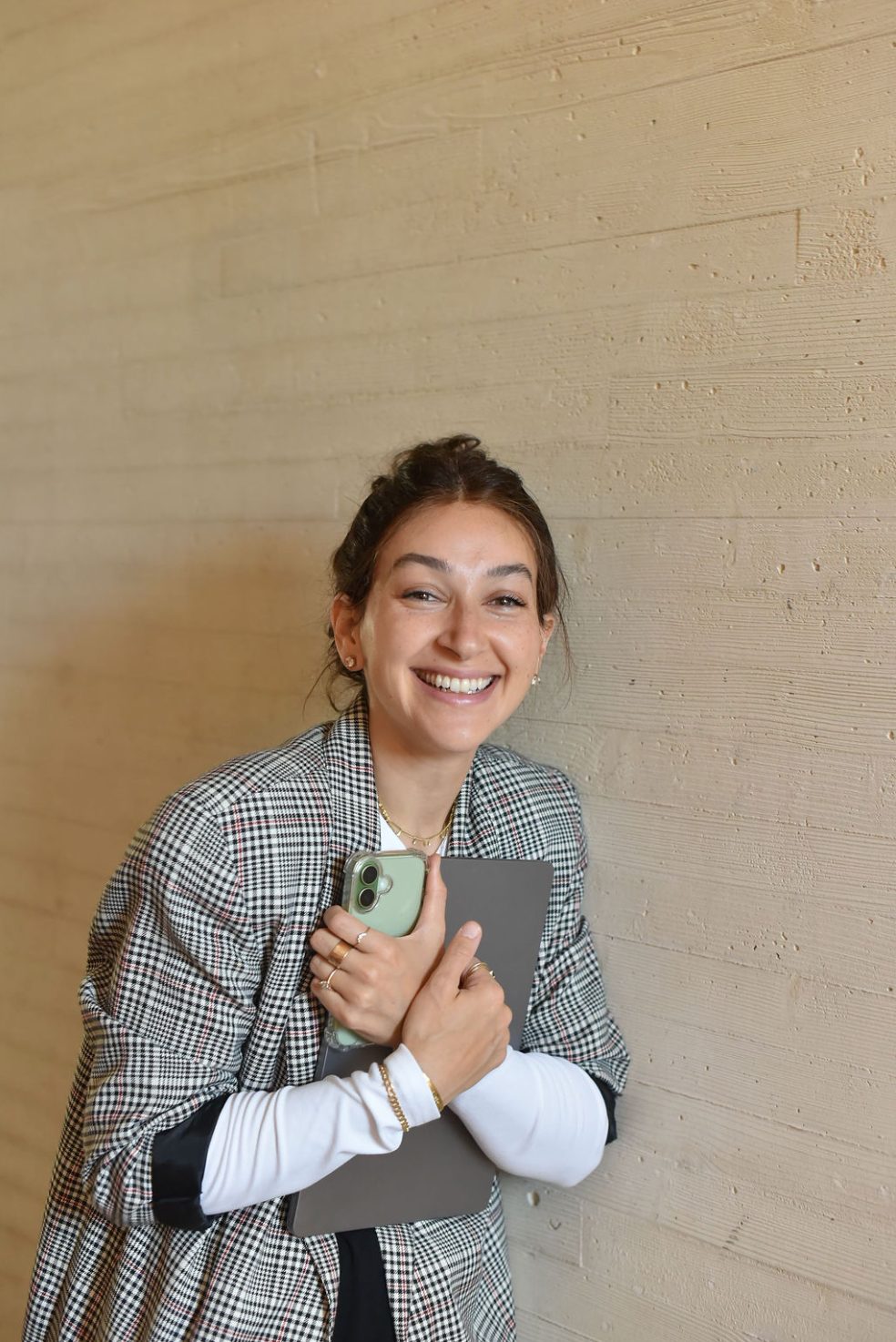 Tova smiling, holding her phone and notebook against a stone wall